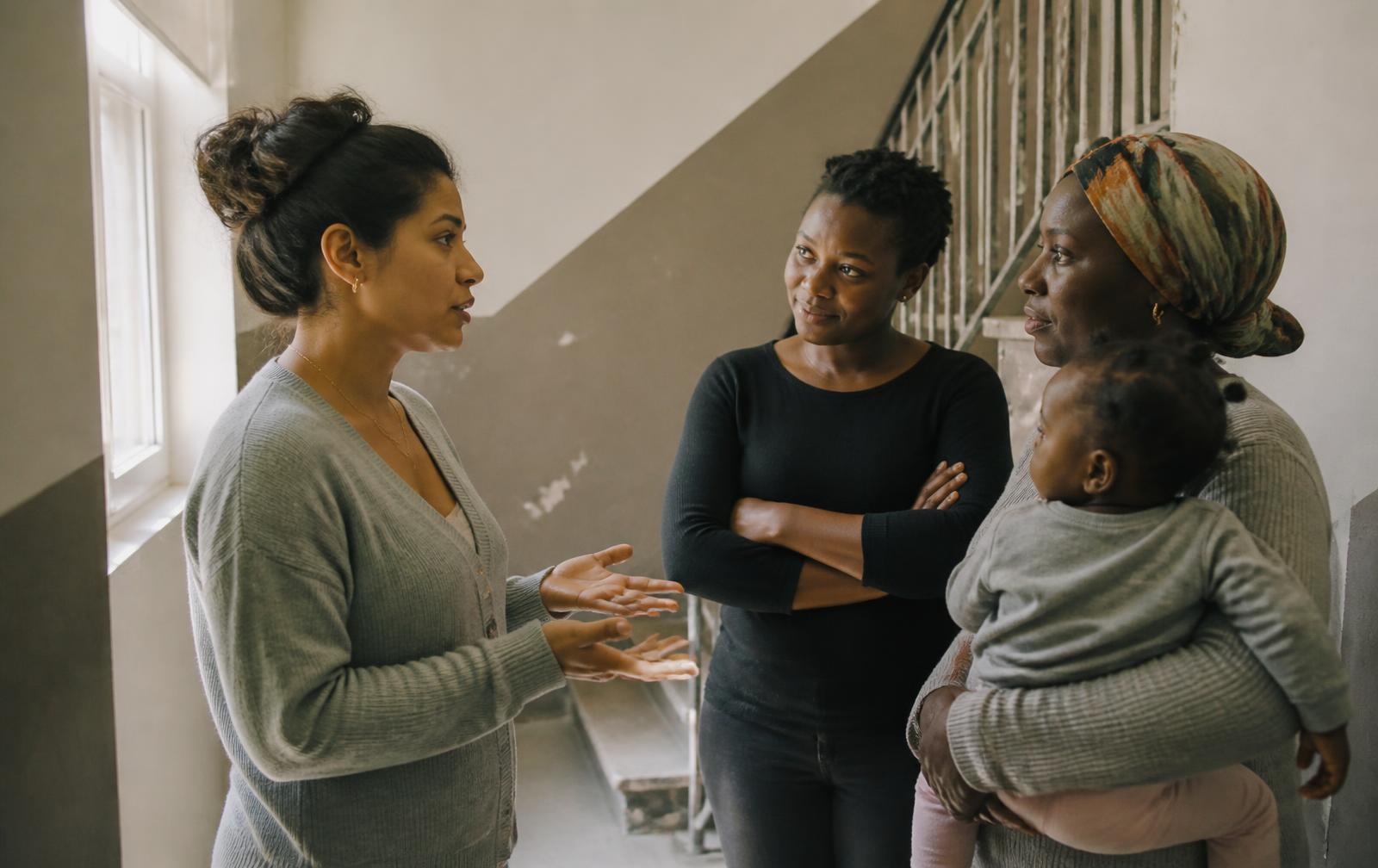 A mother asking two neighbours for advice on an apartment stairwell landing