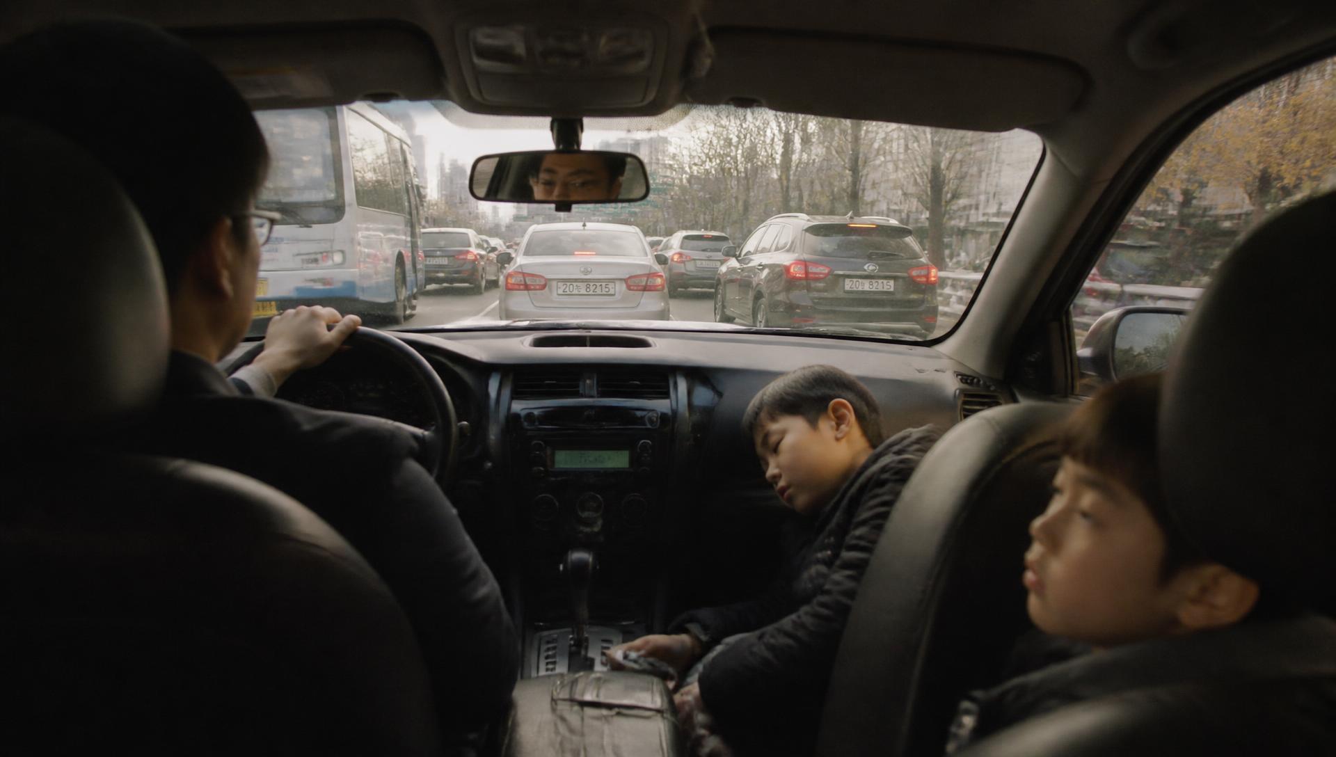 A parent driving two children through slow morning traffic