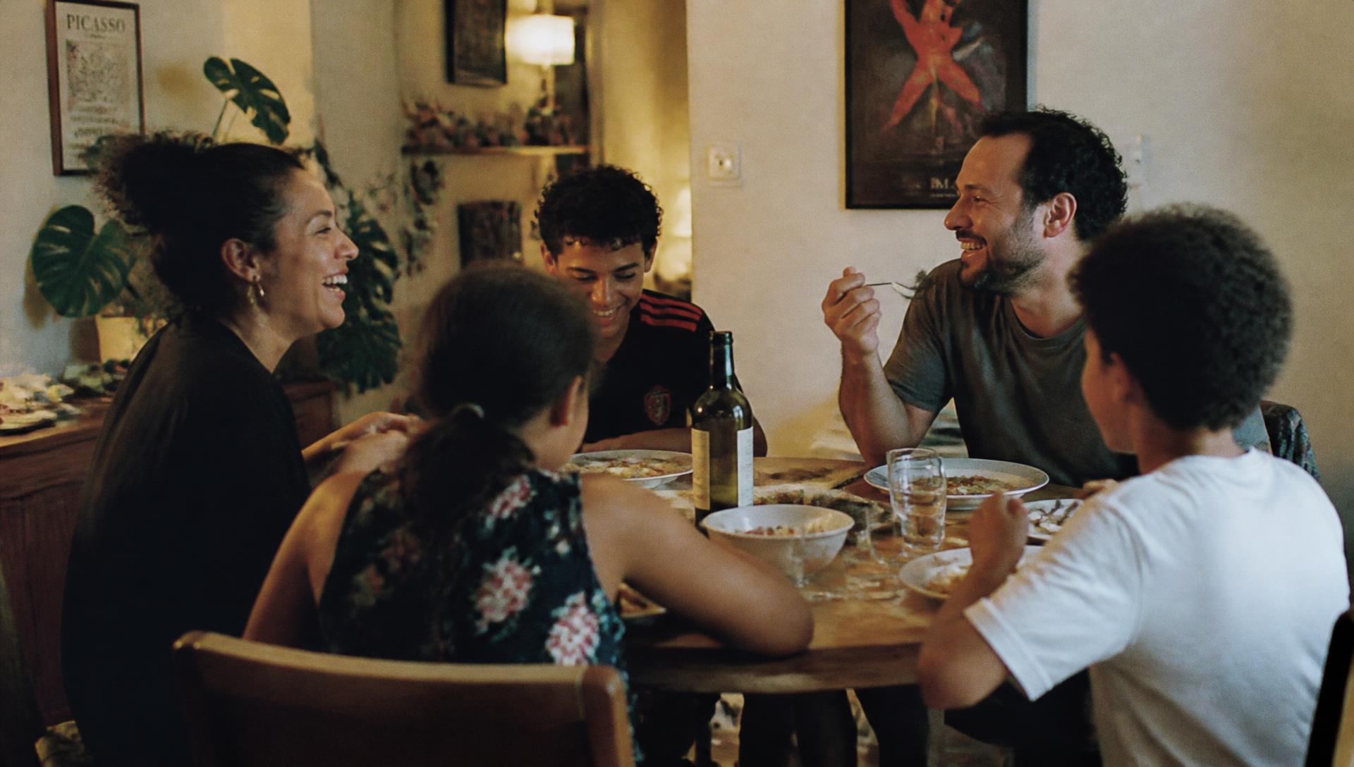 A family of five eating dinner together, laughing mid-conversation