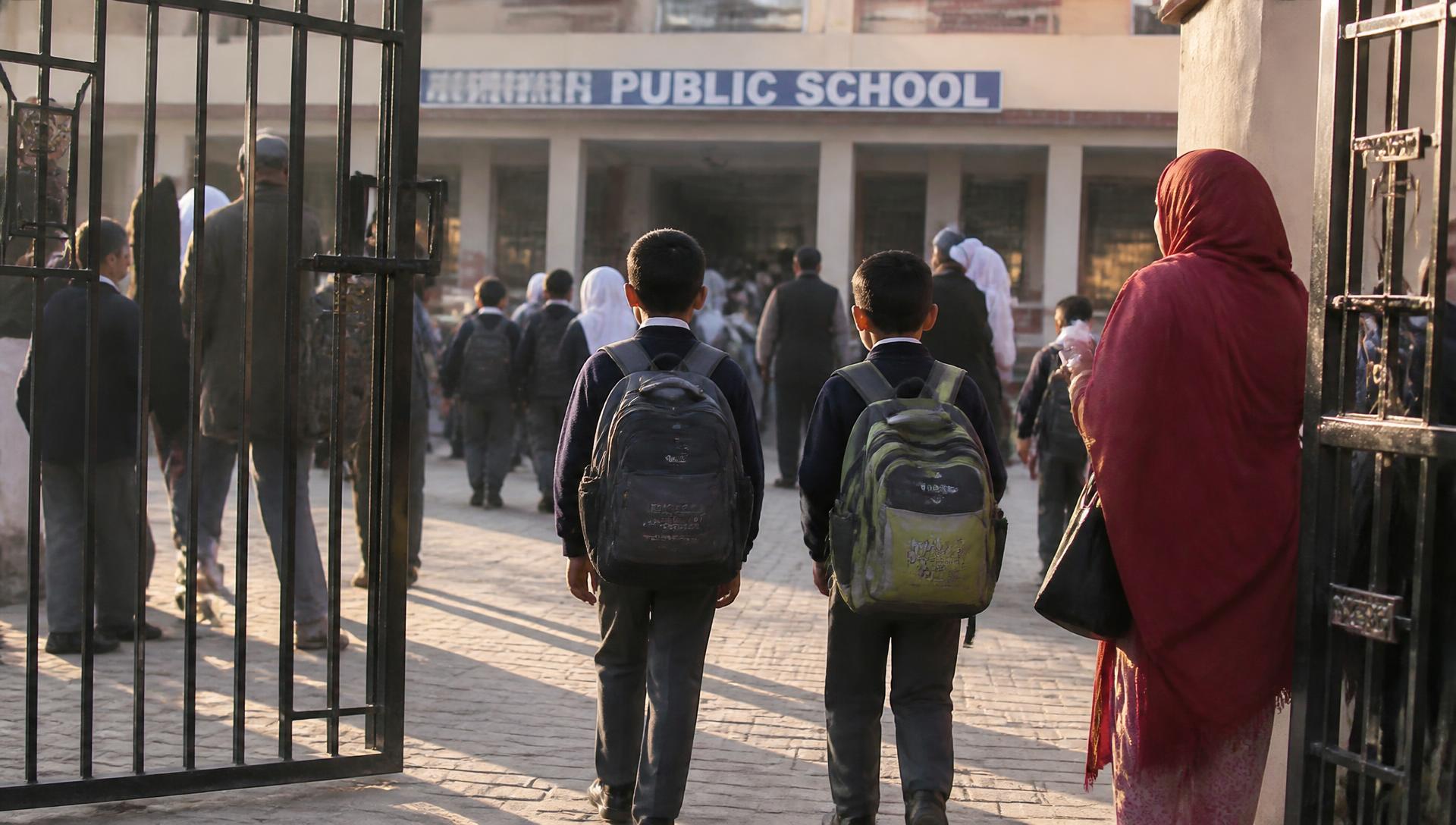 Two children walking through a school gate in early morning light