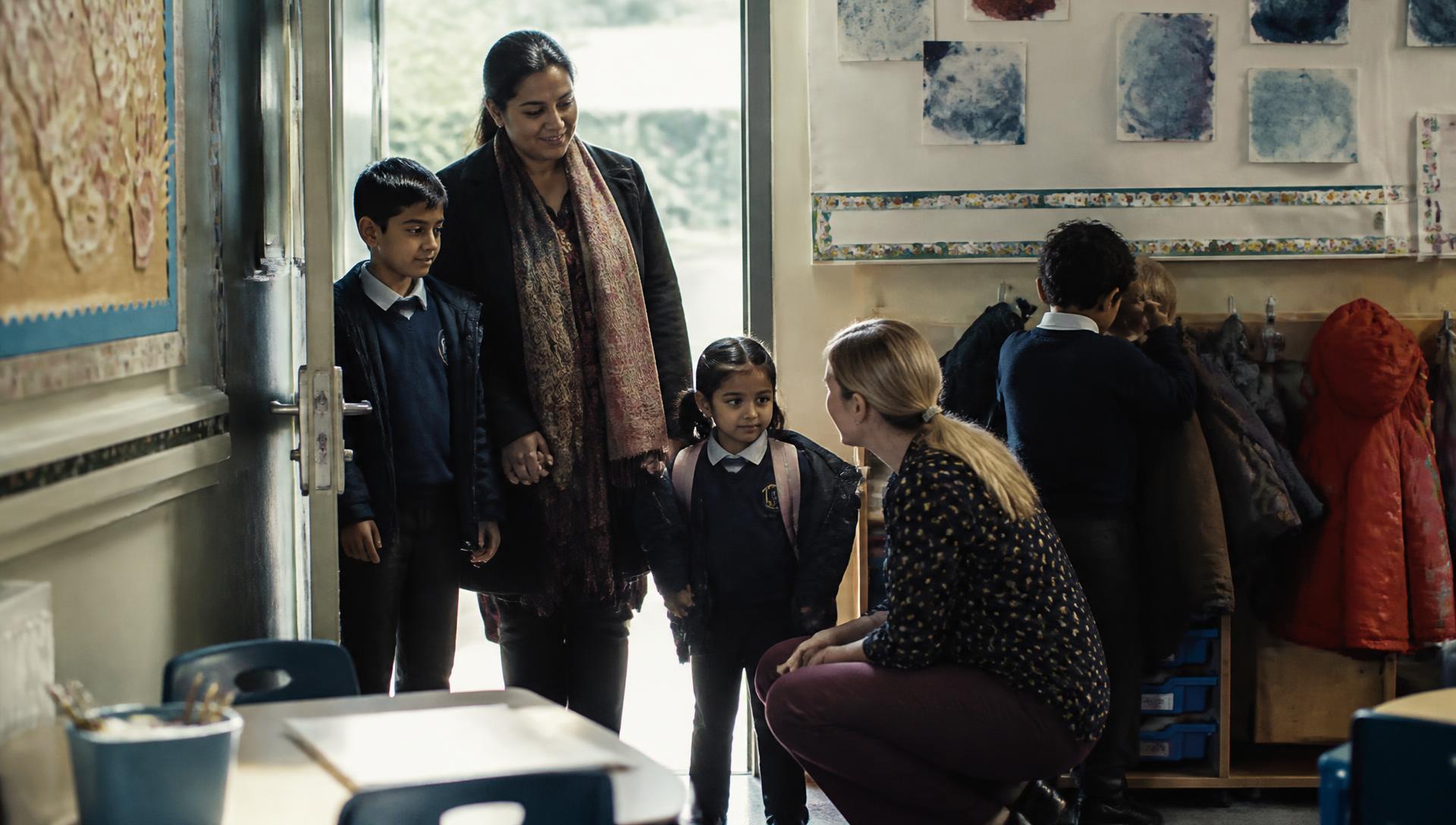 A mother and her two children being welcomed into their new classroom